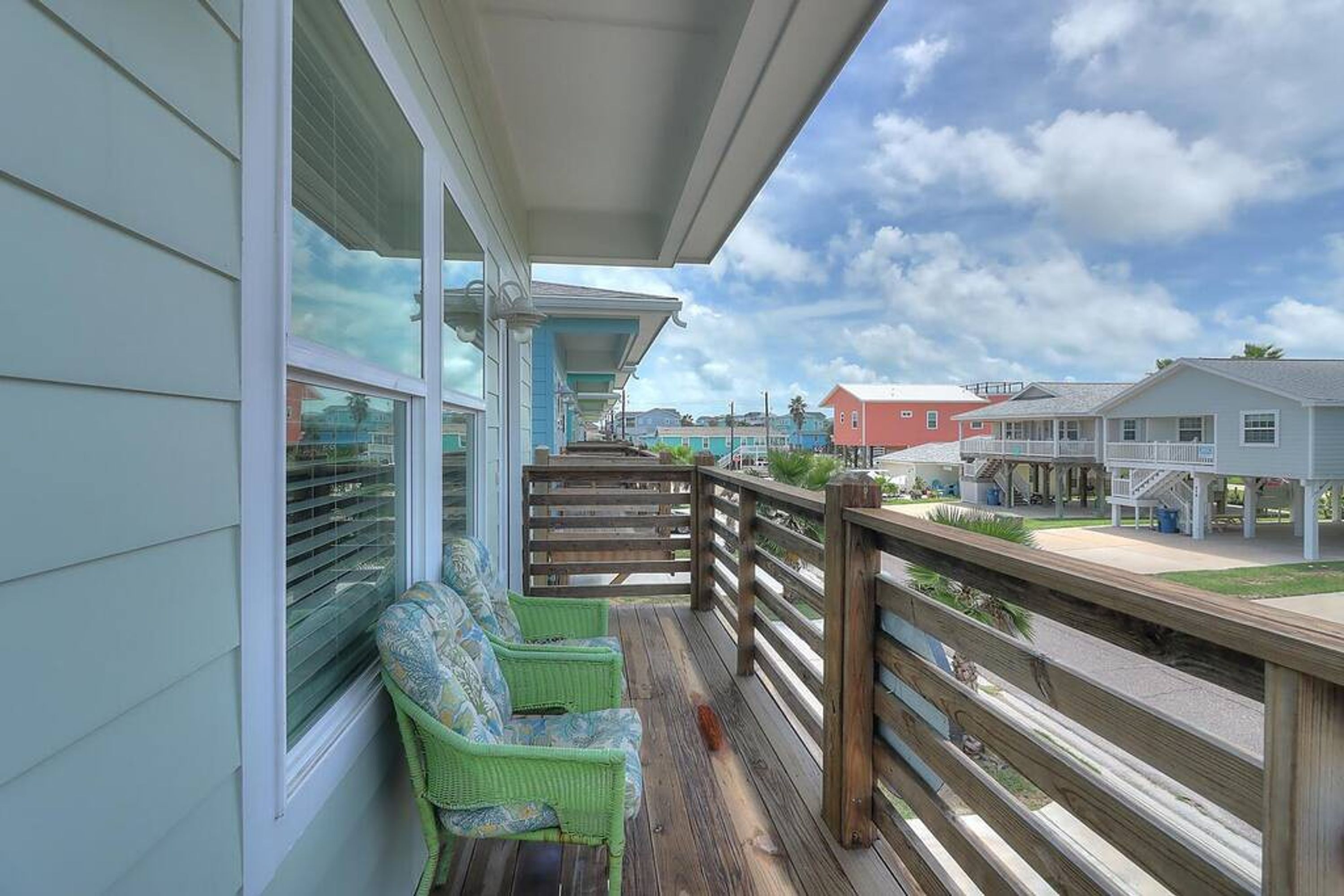A wooden deck with a railing, a covered area with a bench, and a view of houses in the background.