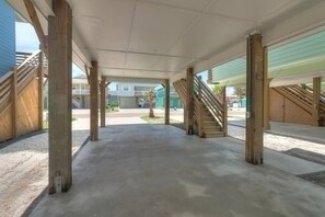 Un espacio abierto cubierto con suelo de concreto, vigas de madera y vista de edificios residenciales al fondo.