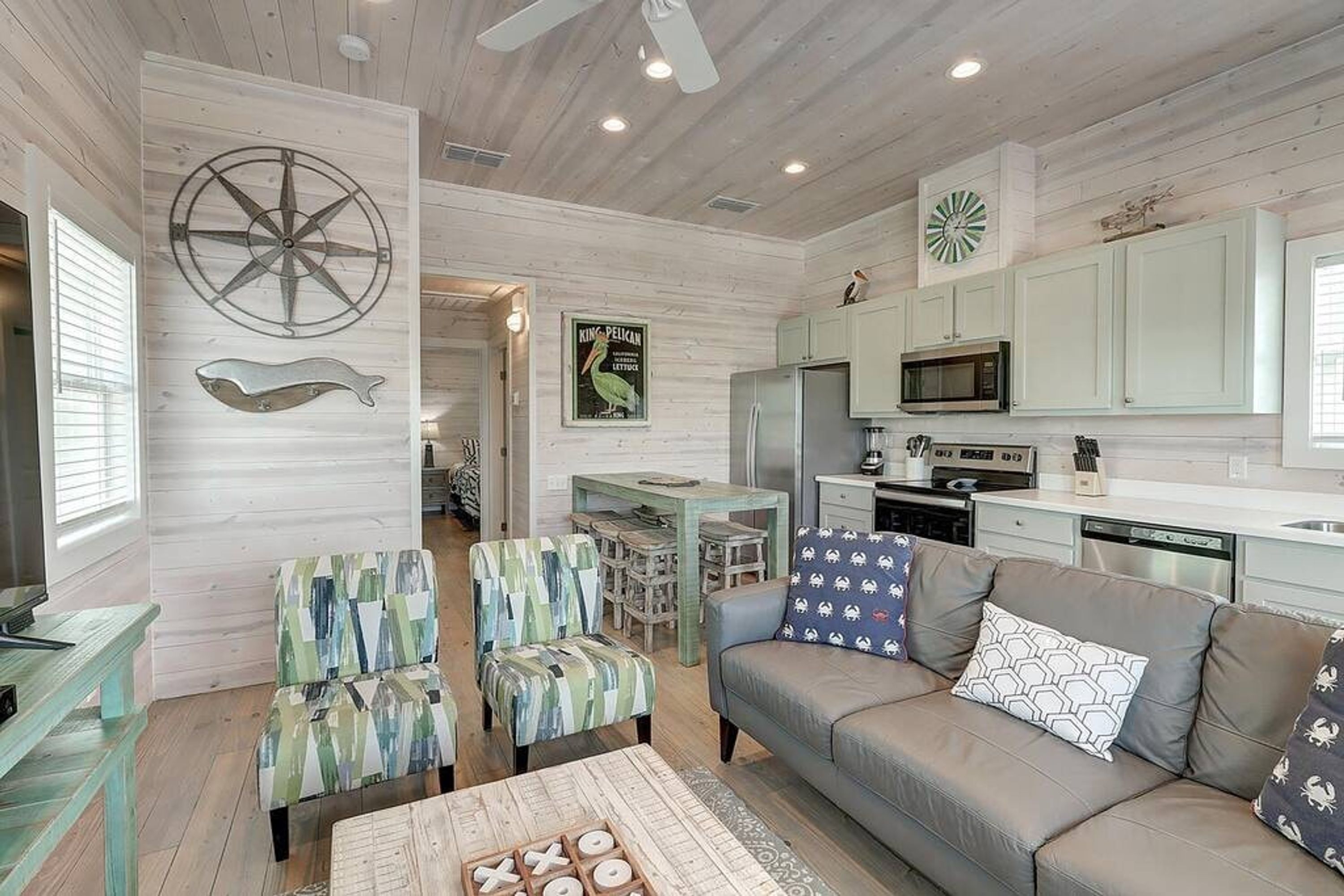 A modern living room with a sofa, armchairs, and a coffee table. There is a kitchen area with a microwave and cabinets.