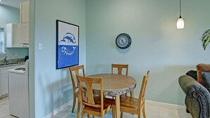 A dining area with a round table and chairs, a clock on the wall, and a kitchen in the background. - Captains Quarters Large Pool Boardwalk to Beach (Port Aransas)