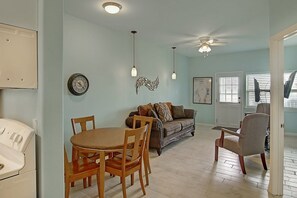 Ein Essbereich mit rundem Tisch und Stühlen, einer Couch mit Kissen, einem Deckenventilator und einer Wanduhr.