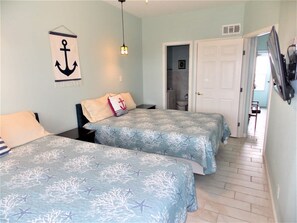 Un dormitorio con dos camas, una lámpara colgante y una puerta que da a un baño.