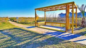 A wooden bench under a pergola with a clear sky in the background. - Captains Quarters Large Pool Boardwalk to Beach (Port Aransas)