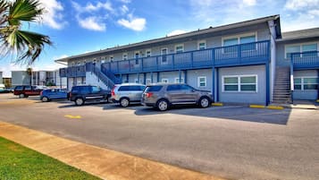 A multi-story motel with a blue exterior, a parking lot with several cars, and a palm tree in the foreground.