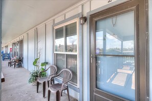 A covered outdoor area with a row of windows, a door with a chain, and two chairs. - Pompano- 2 Min Drive to Beach Sleeps 4 (Port Aransas)