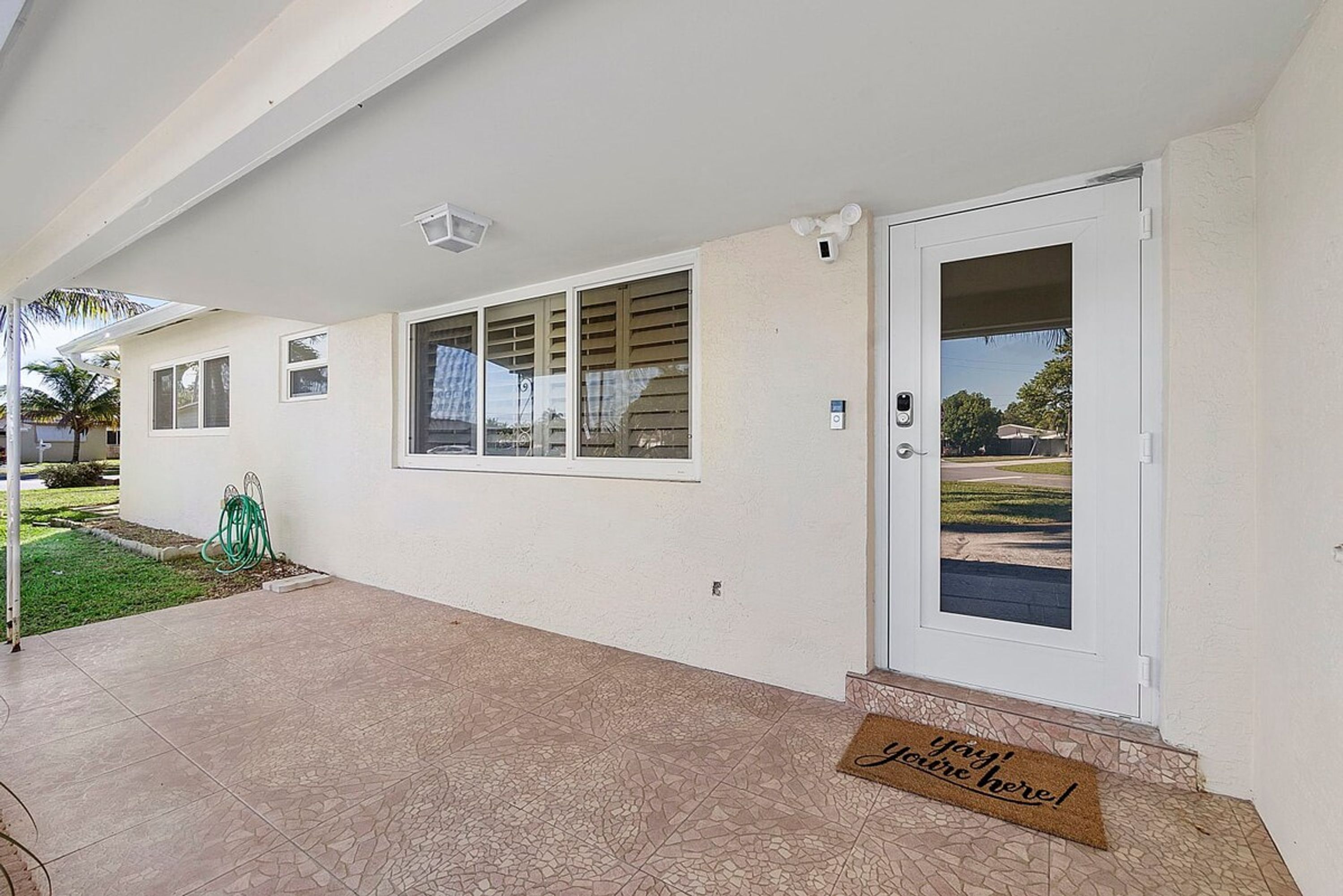 Una casa residencial con porche cubierto, puerta principal y felpudo con un mensaje de bienvenida.