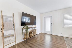 Ein Zimmer mit Holzboden, einem an der Wand montierten Fernseher, einer Tür und einer Bank mit Körben.