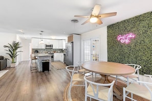 A modern kitchen with white cabinets, a stainless steel refrigerator, and a dining area with a round wooden table and white chairs. - Deerfield Beach 10 min 2 Beach Hot Tub Pool Table (Deerfield Beach)