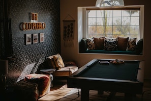 A room with a pool table, a sofa with patterned cushions, a wall with a geometric pattern, and a window with a view of trees. - Casa de Oro 360 Desert Views Pool Spa (Tucson)