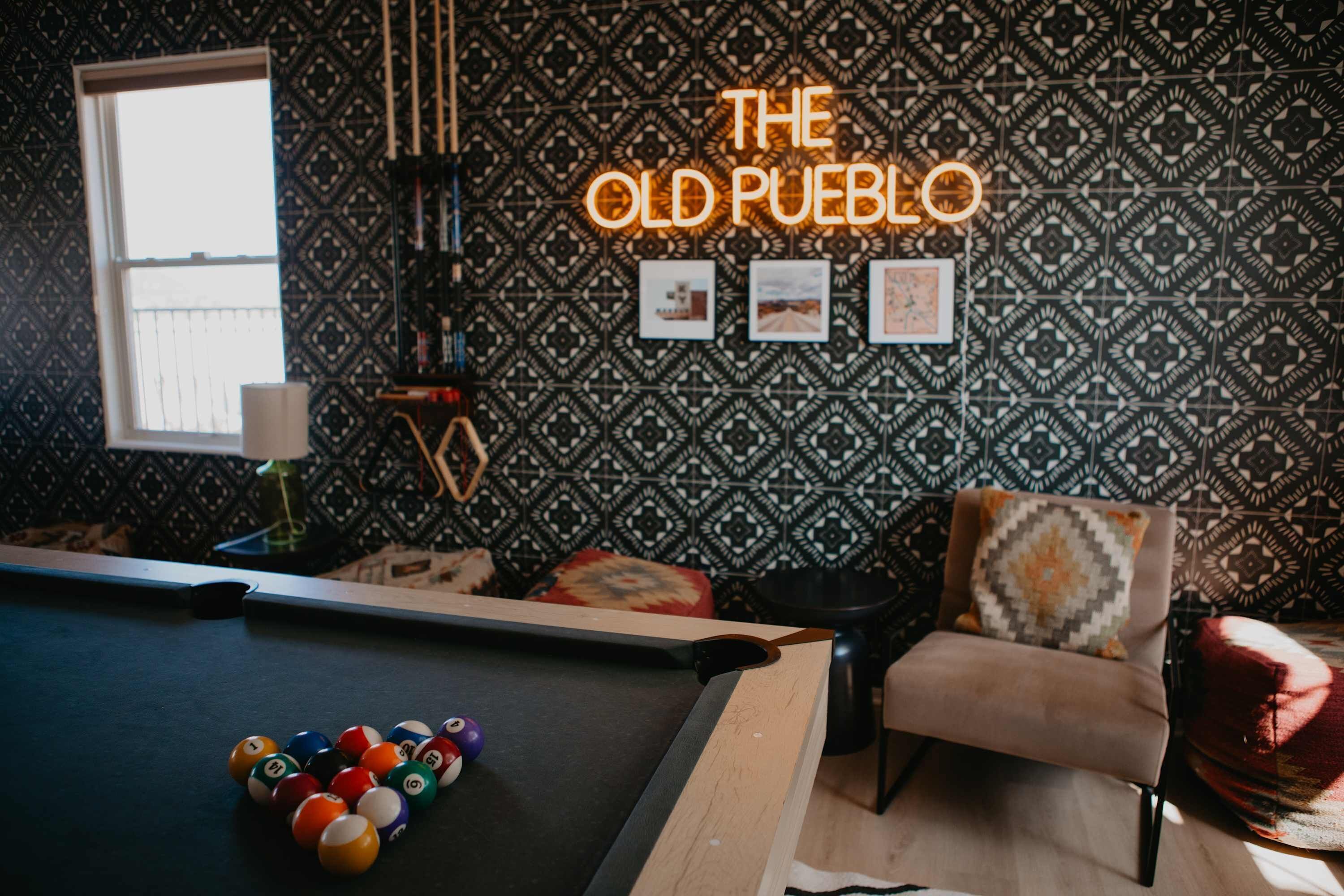 Et billardbord med kugler, et neonskilt med teksten 'THE OLD PUEBLO' og tapet med mønster.