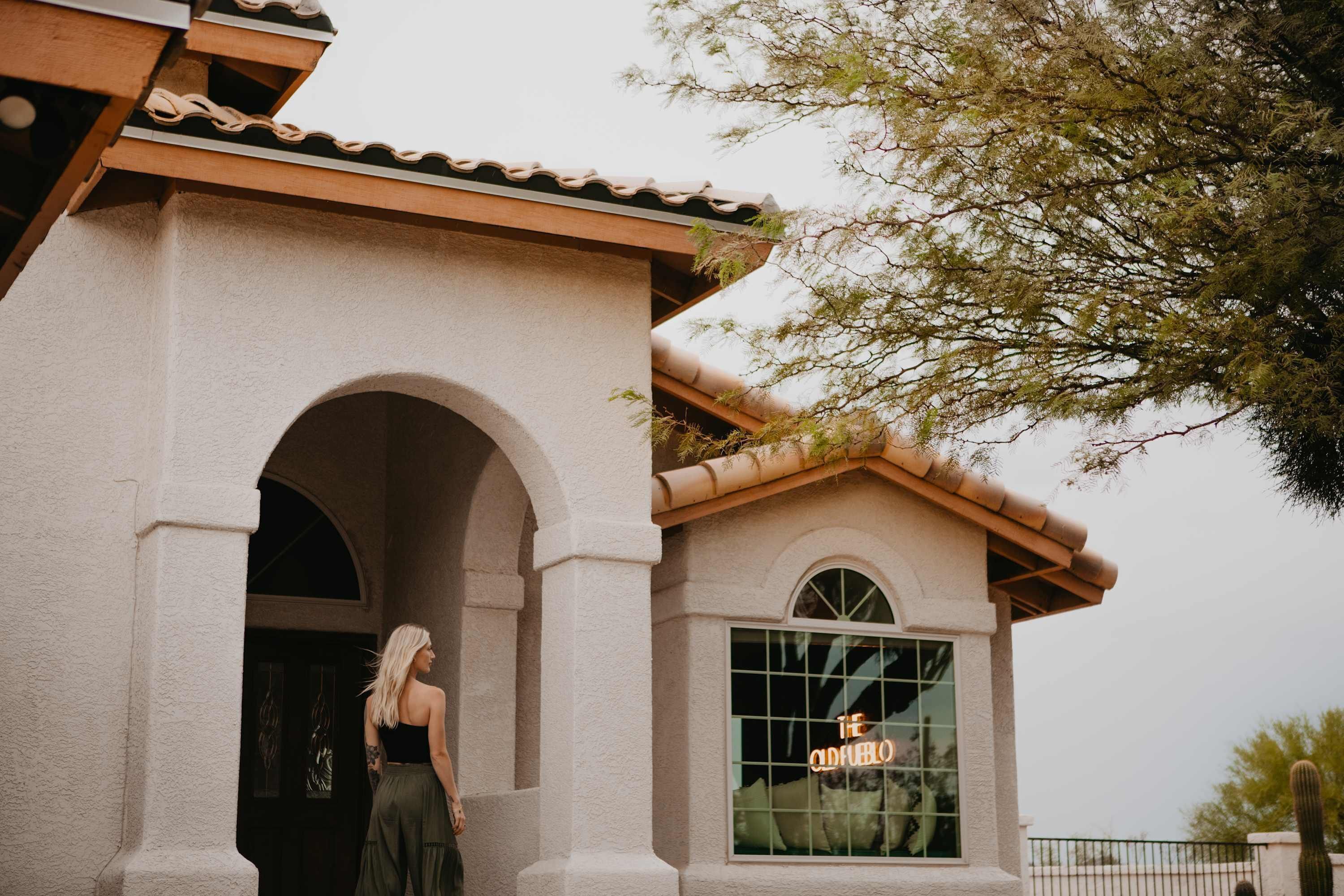 A building with a stucco exterior, an arched doorway, and a large window with a neon sign.