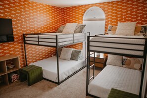 A bunk bed room with orange patterned wallpaper, a television on the left, and a small wooden shelf. - Casa de Oro 360 Desert Views Pool Spa (Tucson)
