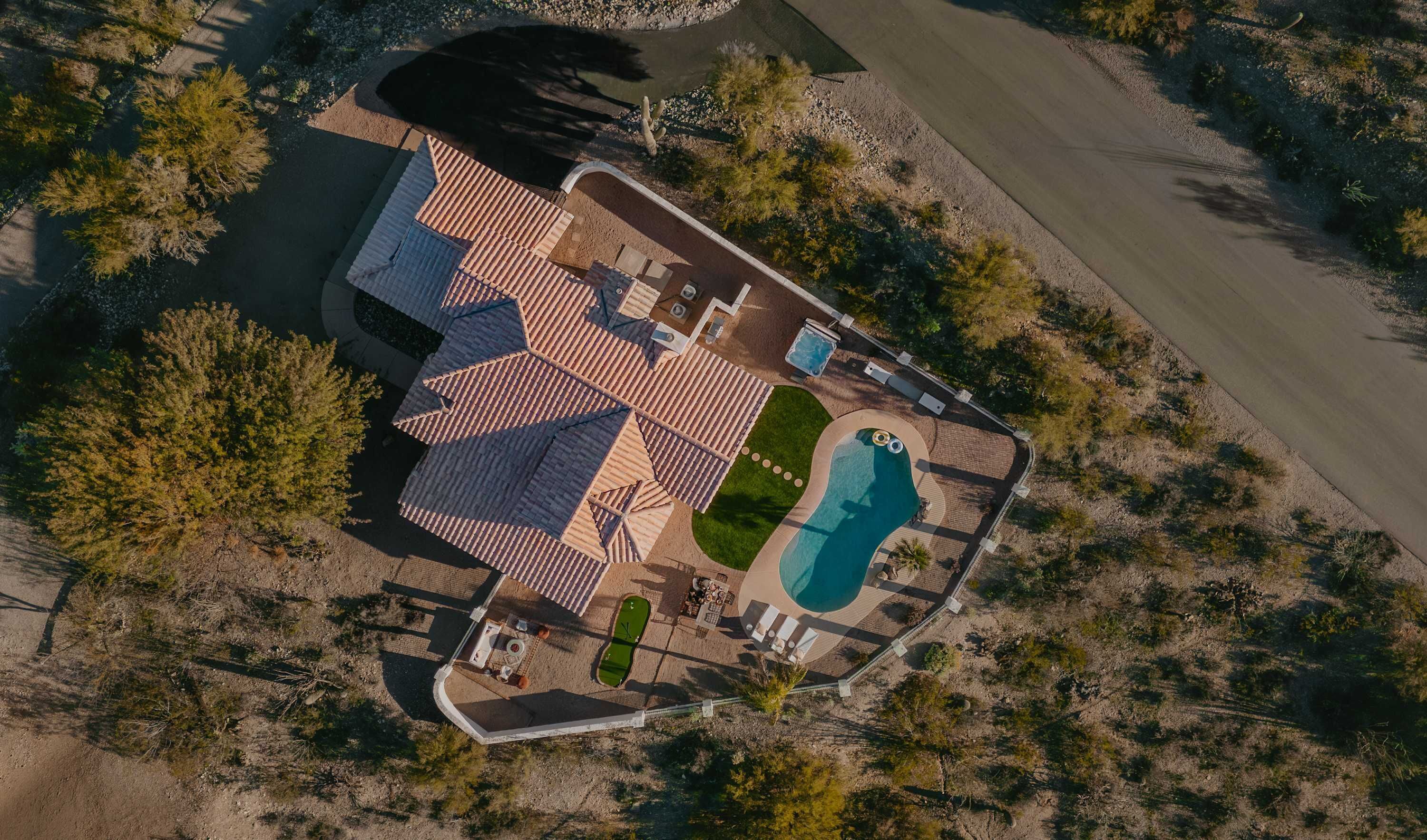 An aerial view of a residential property with a swimming pool, patio area, and a large house with a tiled roof.