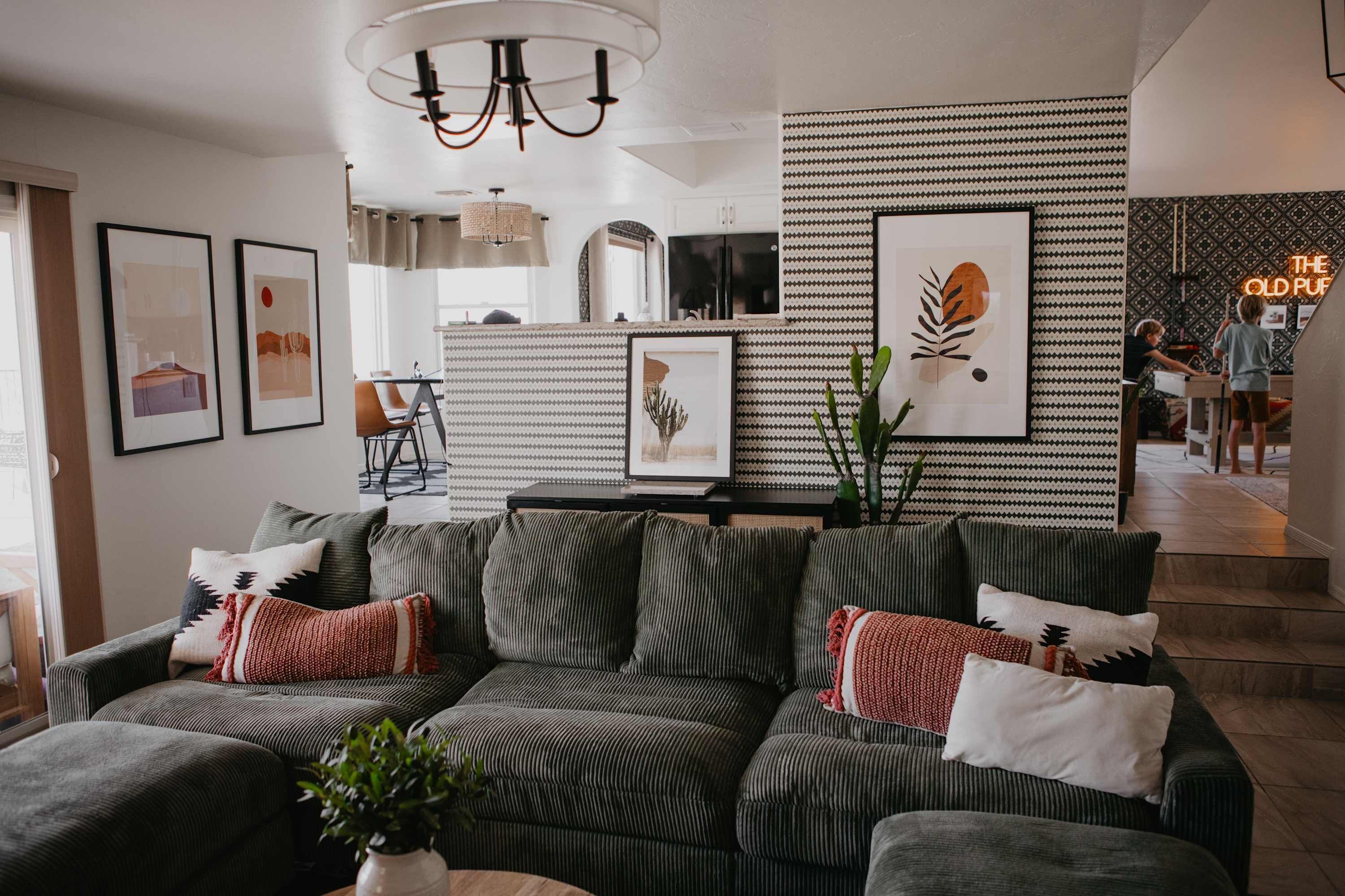 A modern living room with a sofa set, framed artwork, and a kitchen in the background.