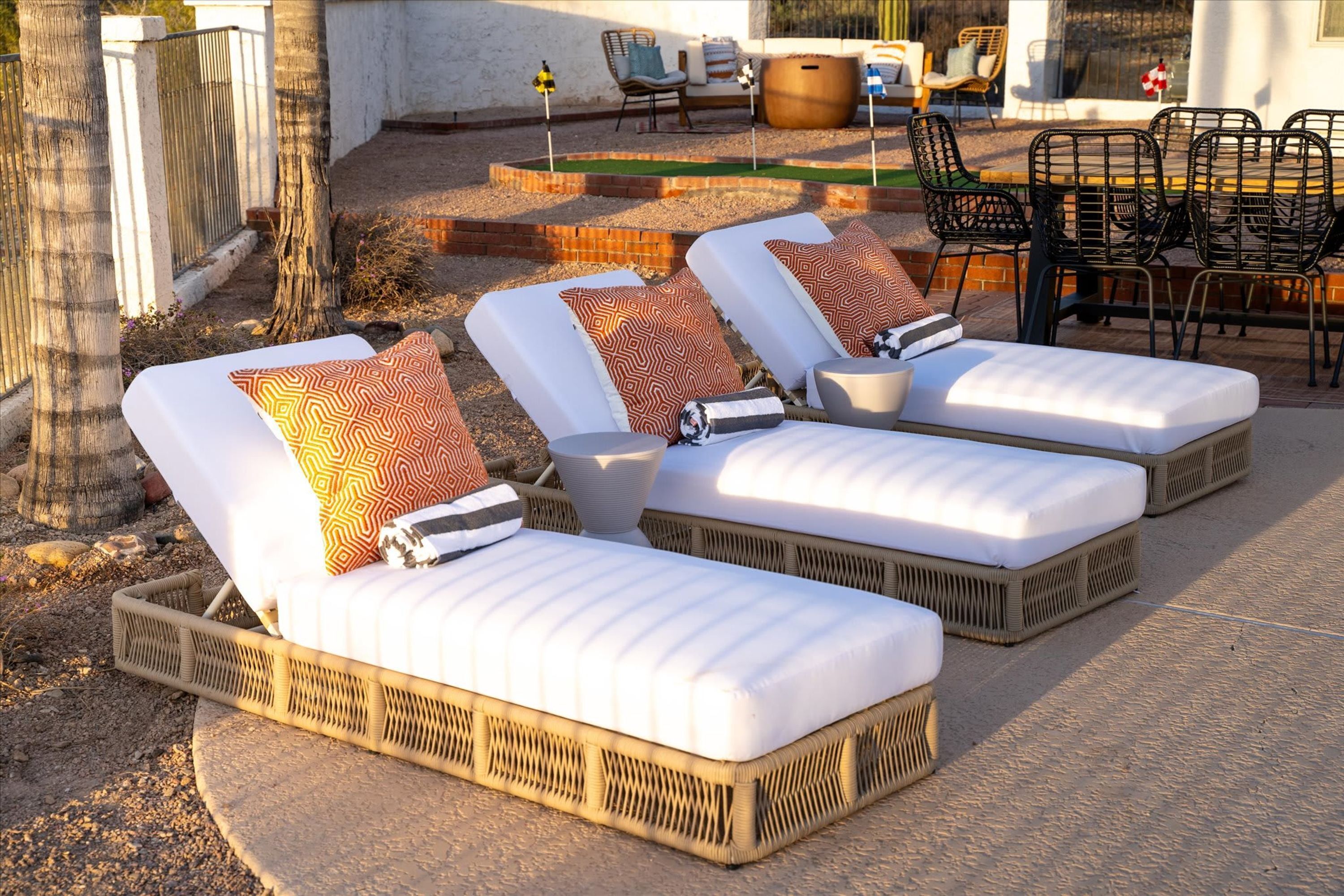 Trois fauteuils de jardin avec coussins, disposés en rangée sur une terrasse bordée de briques.