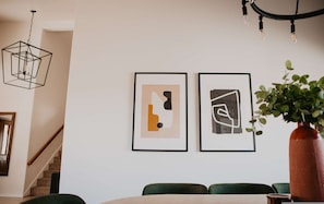 A dining area with a staircase, a hanging light fixture, and two framed abstract artworks on the wall. - Casa de Oro 360 Desert Views Pool Spa (Tucson)