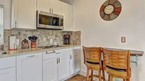 A kitchen with white cabinets, a microwave, a coffee maker, and two wooden chairs. - Siesta Villa Private Patio Dog Friendly Cottage (Port Aransas)