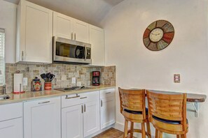 A kitchen with white cabinets, a microwave, a coffee maker, and two wooden chairs. - Siesta Villa Private Patio Dog Friendly Cottage (Port Aransas)
