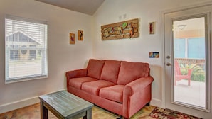 A living room with a red sofa, a wooden coffee table, and a door with a view to the outside. - Siesta Villa Private Patio Dog Friendly Cottage (Port Aransas)