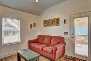 A living room with a red sofa, a wooden coffee table, and a door with a view to the outside. - Siesta Villa Private Patio Dog Friendly Cottage (Port Aransas)