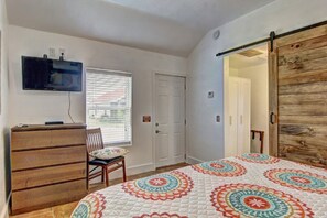 A bedroom with a bed, a dresser, a television, a window with blinds, and a door. - Siesta Villa Private Patio Dog Friendly Cottage (Port Aransas)