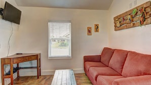 A living room with a wooden coffee table, a red sofa, a television mounted on the wall, and a window with blinds. - Siesta Villa Private Patio Dog Friendly Cottage (Port Aransas)