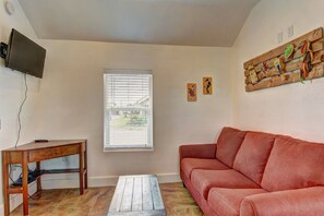 A living room with a wooden coffee table, a red sofa, a television mounted on the wall, and a window with blinds. - Siesta Villa Private Patio Dog Friendly Cottage (Port Aransas)