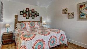 A bedroom with a wooden headboard, a patterned bedspread, two bedside lamps, and wall art. - Siesta Villa Private Patio Dog Friendly Cottage (Port Aransas)