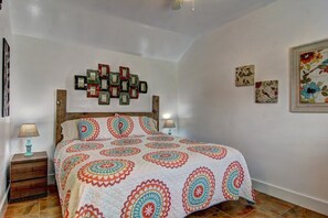 A bedroom with a wooden headboard, a patterned bedspread, two bedside lamps, and wall art. - Siesta Villa Private Patio Dog Friendly Cottage (Port Aransas)