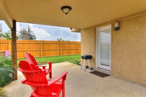 A covered patio area with a concrete floor, a wooden fence in the background, and a sliding glass door. - Siesta Villa Private Patio Dog Friendly Cottage (Port Aransas)
