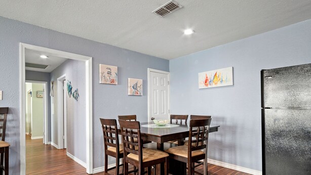 Comedor con mesa y sillas de madera, un refrigerador y obras de arte en las paredes.