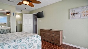 Un dormitorio con cama, cómoda, ventilador de techo, televisor y una puerta.