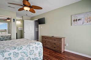 Ein Schlafzimmer mit Bett, Kommode, Deckenventilator, Fernseher und einer Tür.