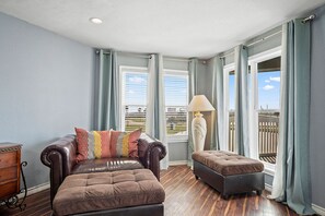Ein Zimmer mit Ledersofa, Hocker, einer Lampe und Blick auf einen Balkon mit Geländer.
