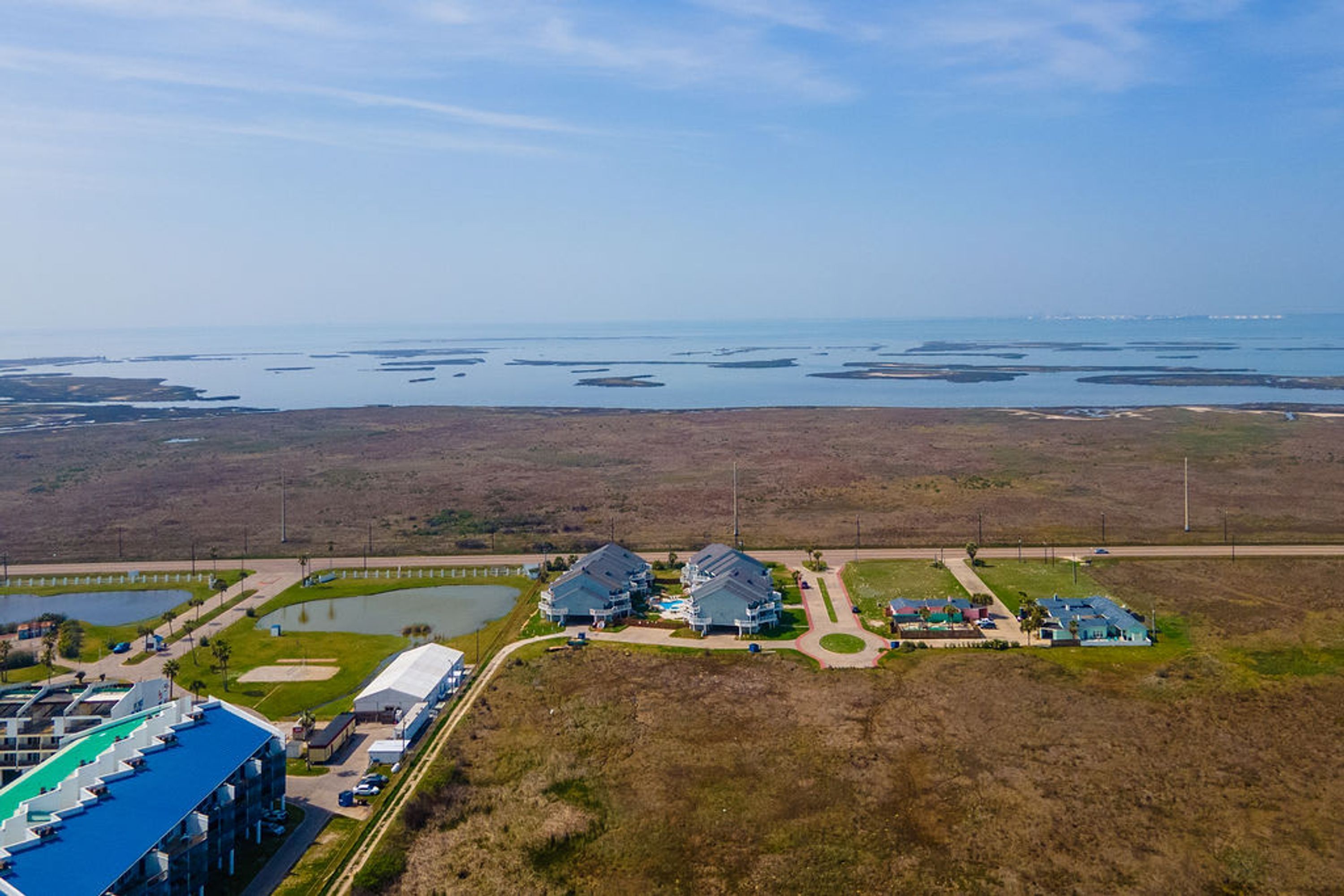 An aerial view of a coastal area with a large building complex, including a parking lot and a swimming pool.