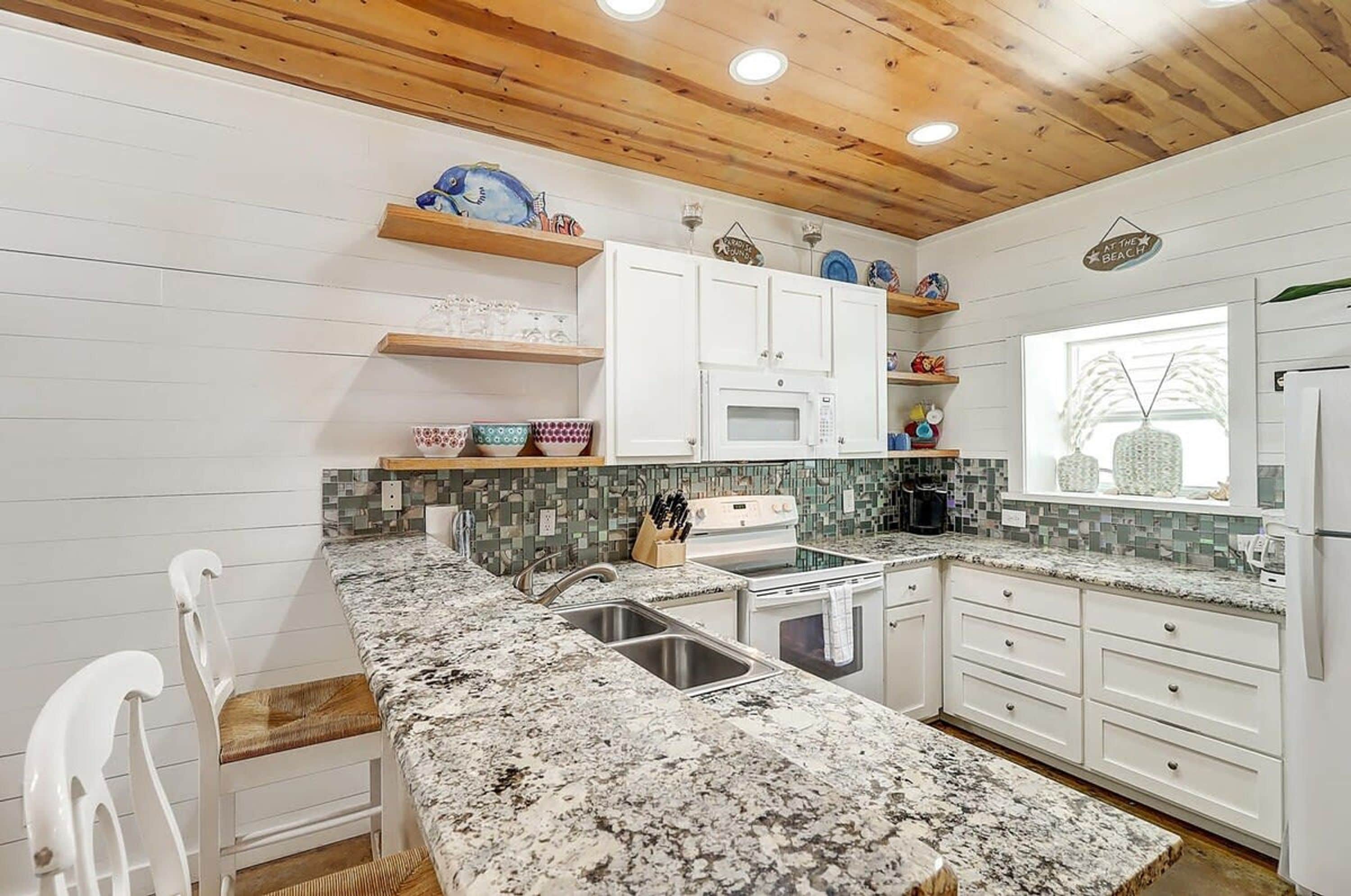 A kitchen with white cabinets, a granite countertop, and a wooden ceiling.