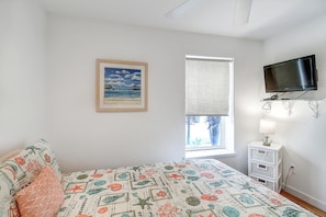 A bedroom with a bed, a television mounted on the wall, a window with a view of the outdoors, and a framed picture on the wall. - Reel Paradise Community Pool Sleeps 10 (Port Aransas)