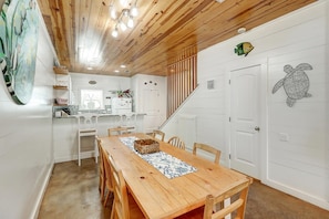A wooden dining table with chairs, a kitchen area with white cabinets, and a staircase leading to another level. - Reel Paradise Community Pool Sleeps 10 (Port Aransas)