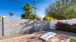 Un patio con pared de concreto, un banco blanco y un pequeño jardín con flores rojas.