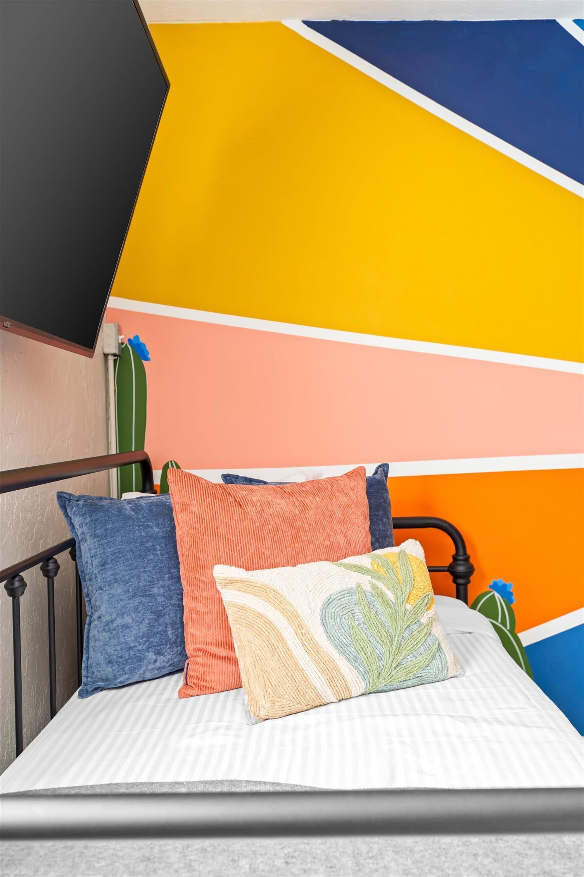Un lit avec un matelas à rayures, une structure en m étal et des coussins colorés.