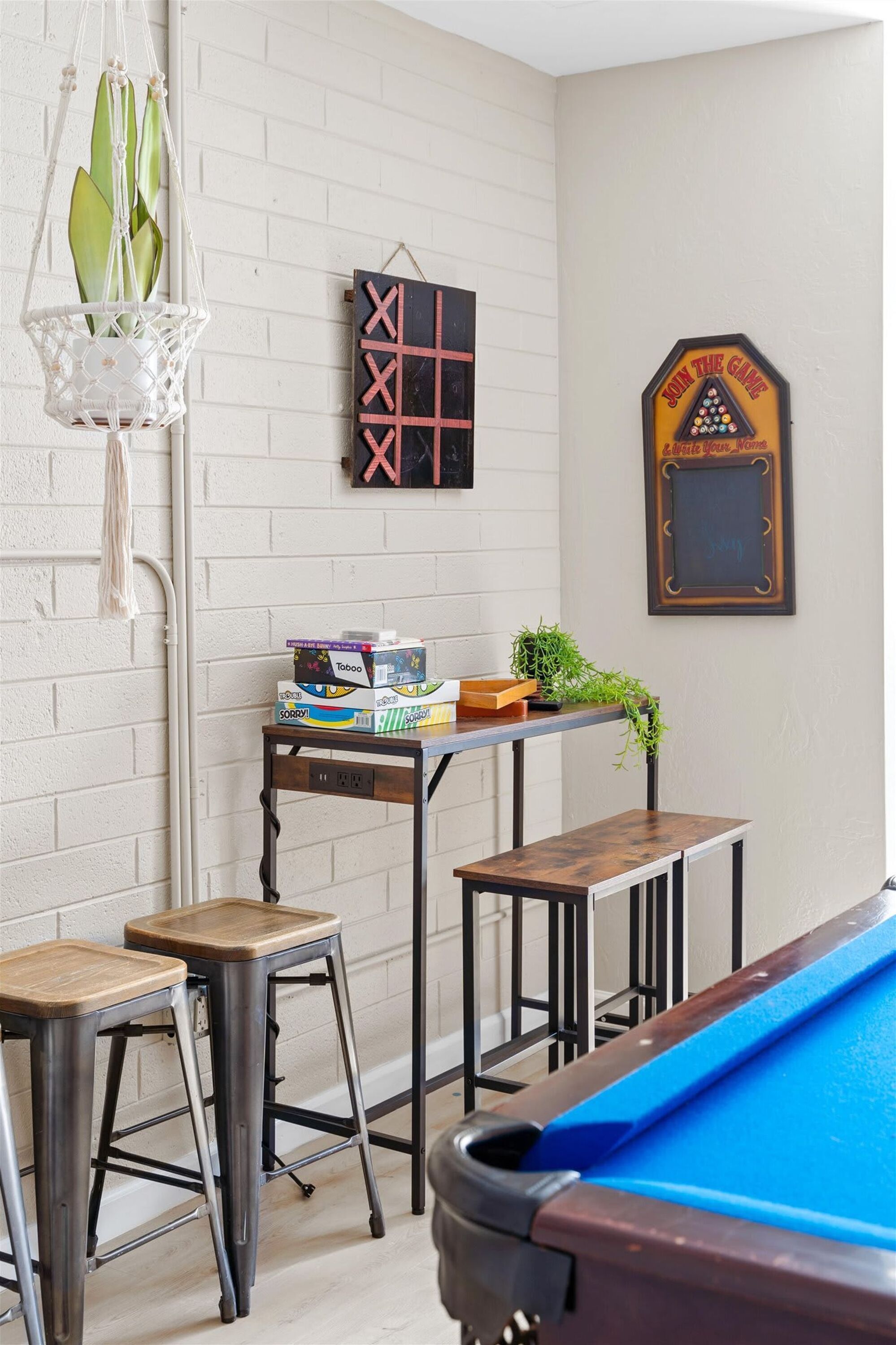 A pool table with stools, a small table with board games, and a wall-mounted decoration.