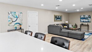 Una sala moderna con un sofá seccional gris, una mesa de comedor con sillas y obras de arte en las paredes.