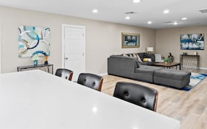 Ein modernes Wohnzimmer mit einem grauen Ecksofa, einem Esstisch mit Stühlen und Bildern an den Wänden.