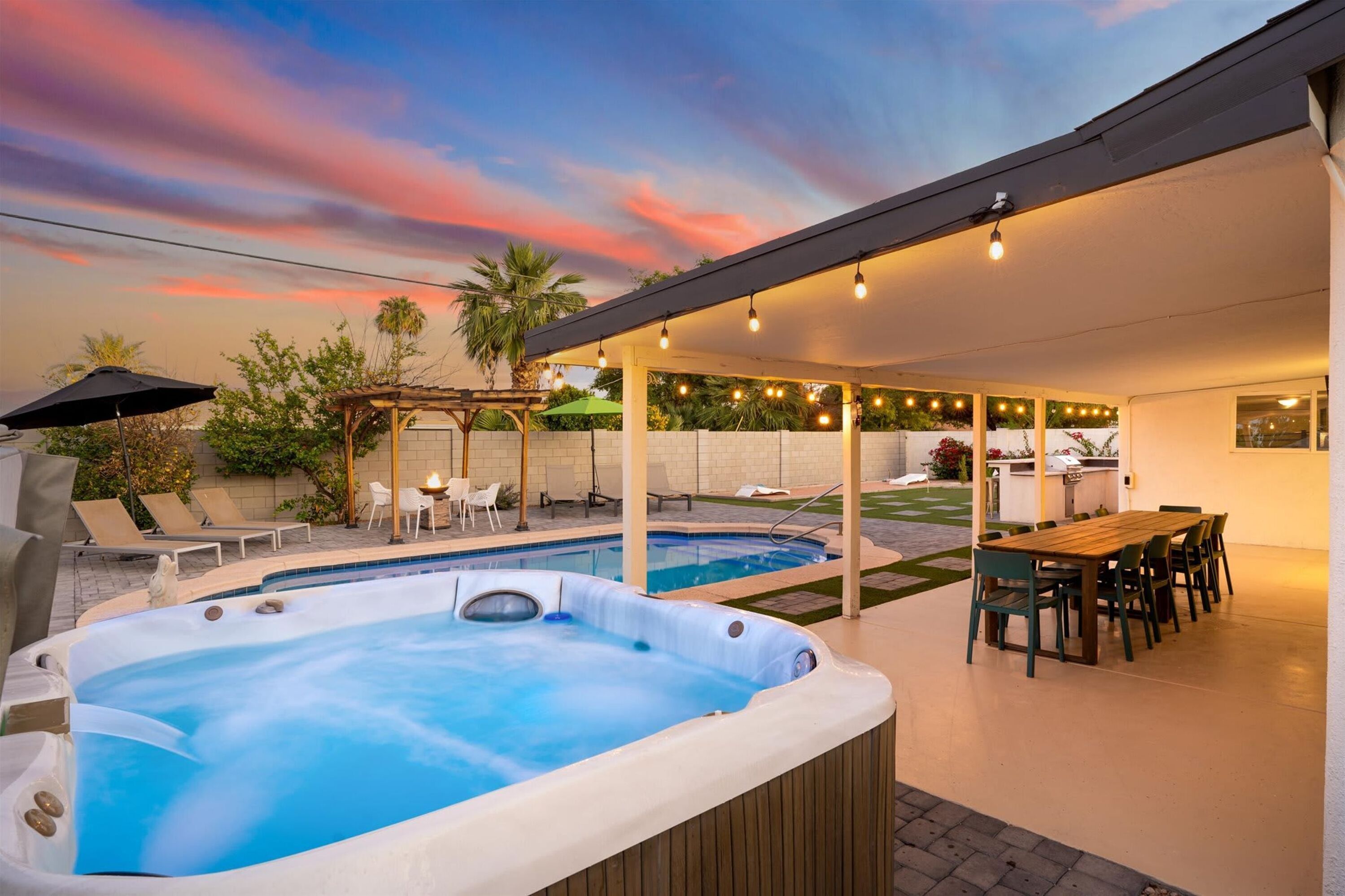 Un jardin avec un jacuzzi, une piscine, du mobilier d’extérieur et des guirlandes lumineuses.