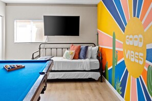 Ein Zimmer mit einem Bett, einem Billardtisch und einer Wand mit einem farbenfrohen Wandgemälde.