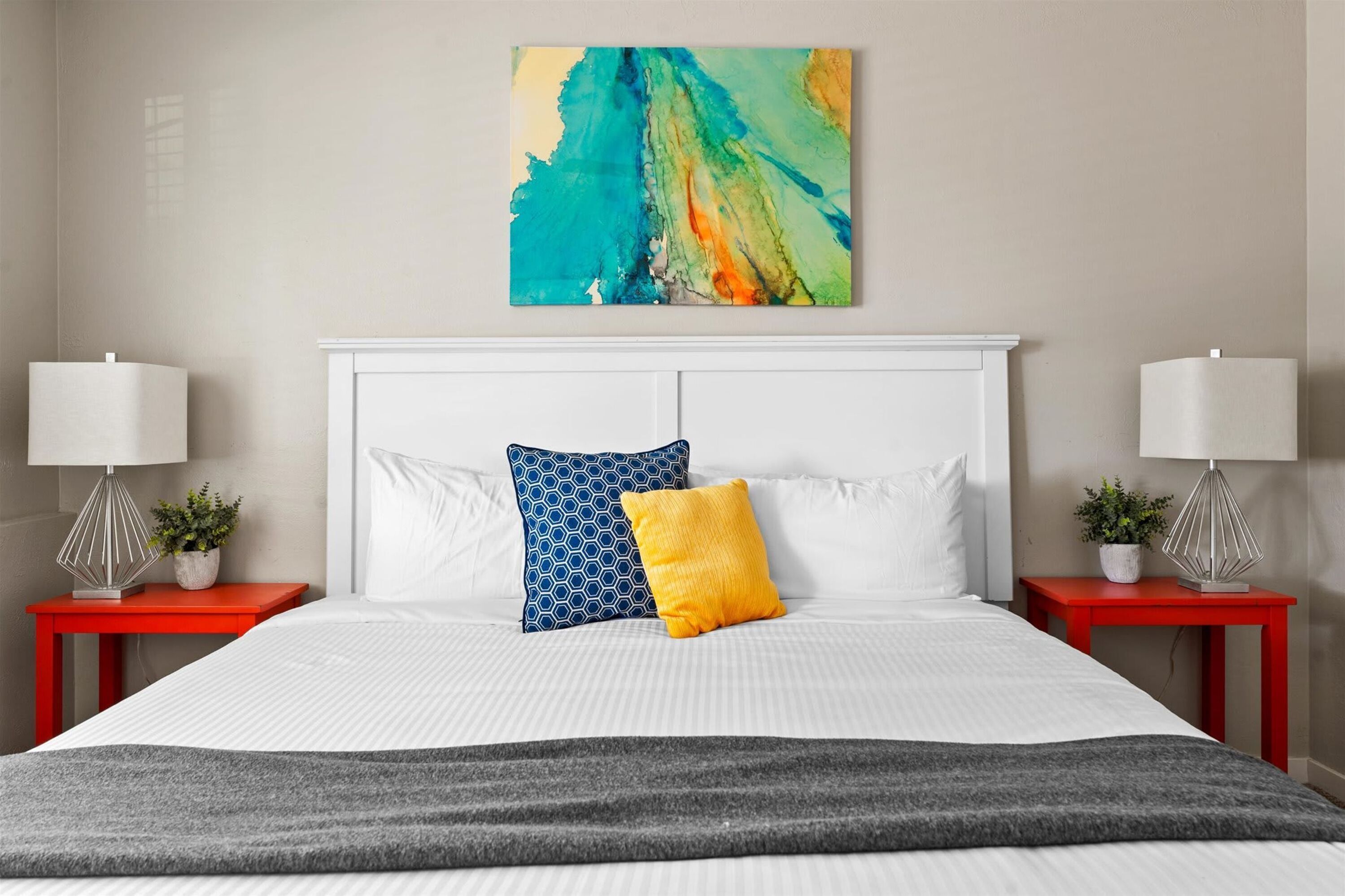 Una habitació d'hotel amb un llit gran, dues taules de nit, dues làmpades i un quadre abstracte i colorit a la paret.