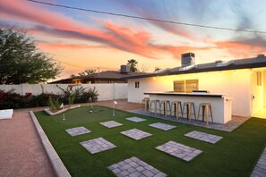 Un patio con césped artificial, un campo de práctica de golf y una zona de bar con taburetes.