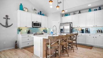 Una cocina moderna con armarios blancos, una isla central, sillas de madera e iluminación colgante.