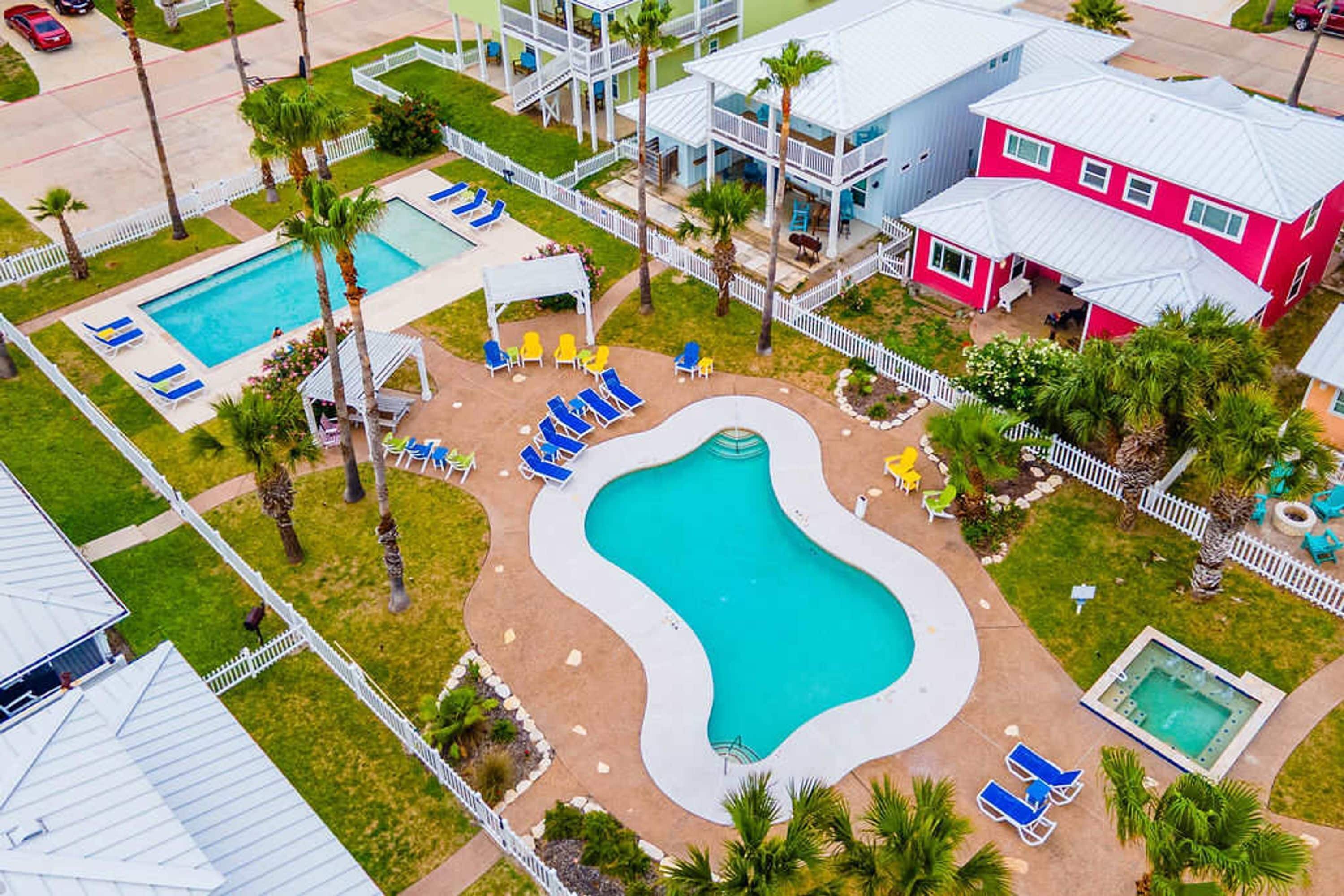 A residential area with a swimming pool, lounge chairs, and a pink house.