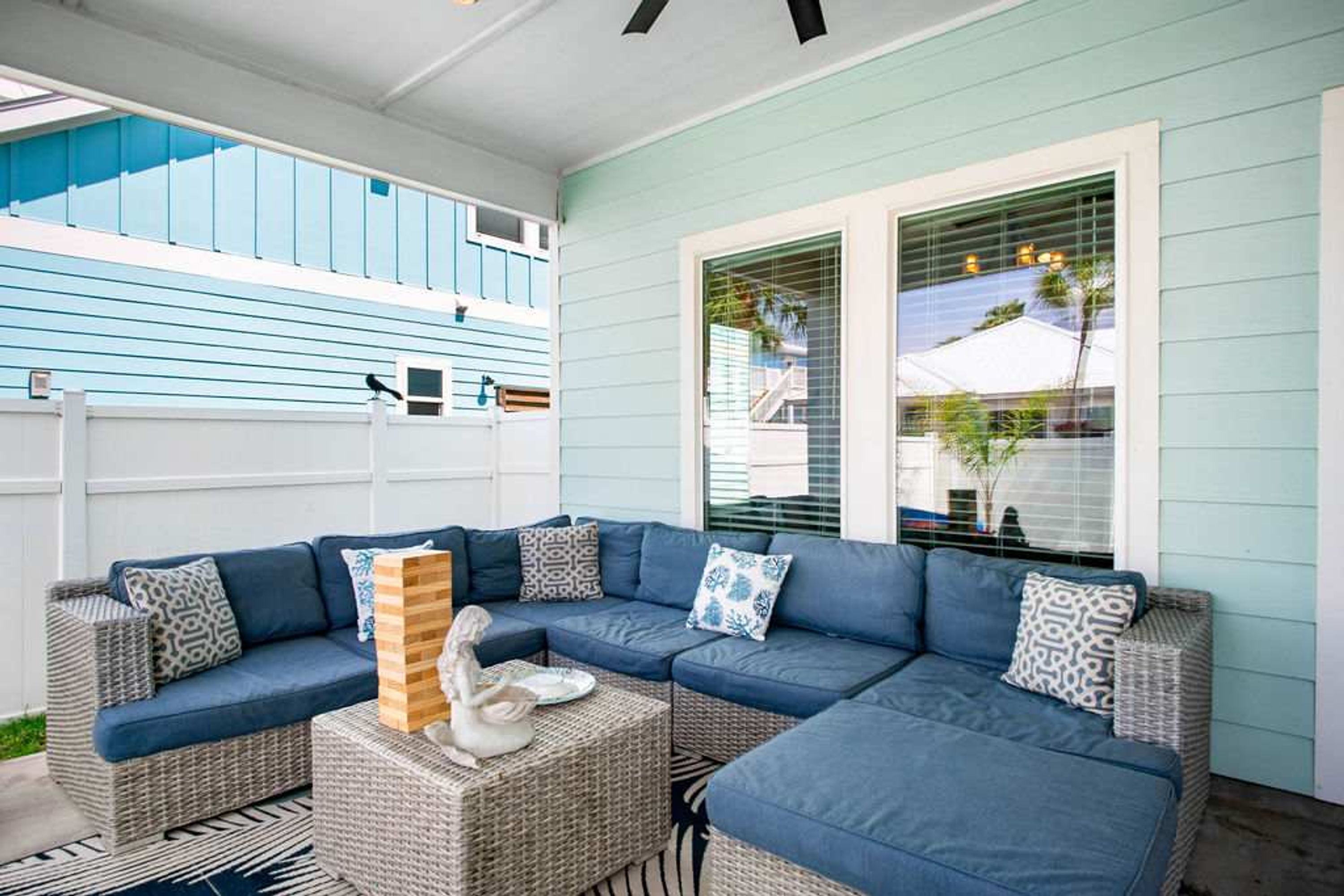 A covered outdoor seating area with a sectional sofa, wicker ottomans, and a decorative swan statue.